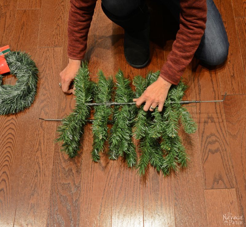 woman placing a fake christmas tree branch on top of another