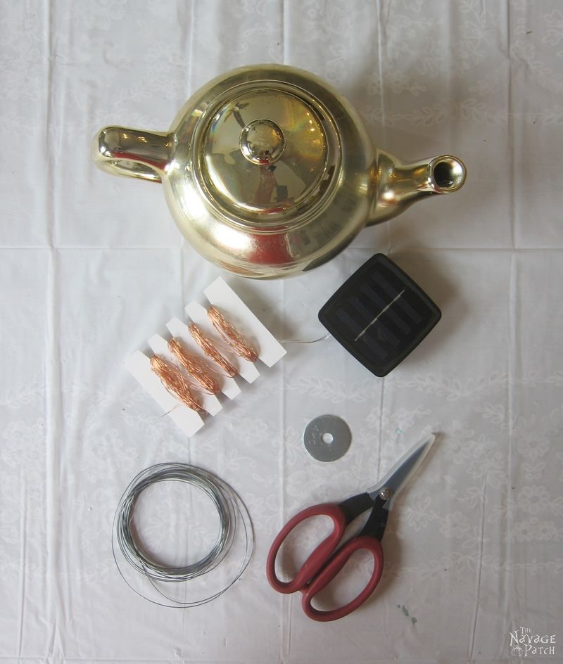 teapot, solar string lights, wire and scissors on a table