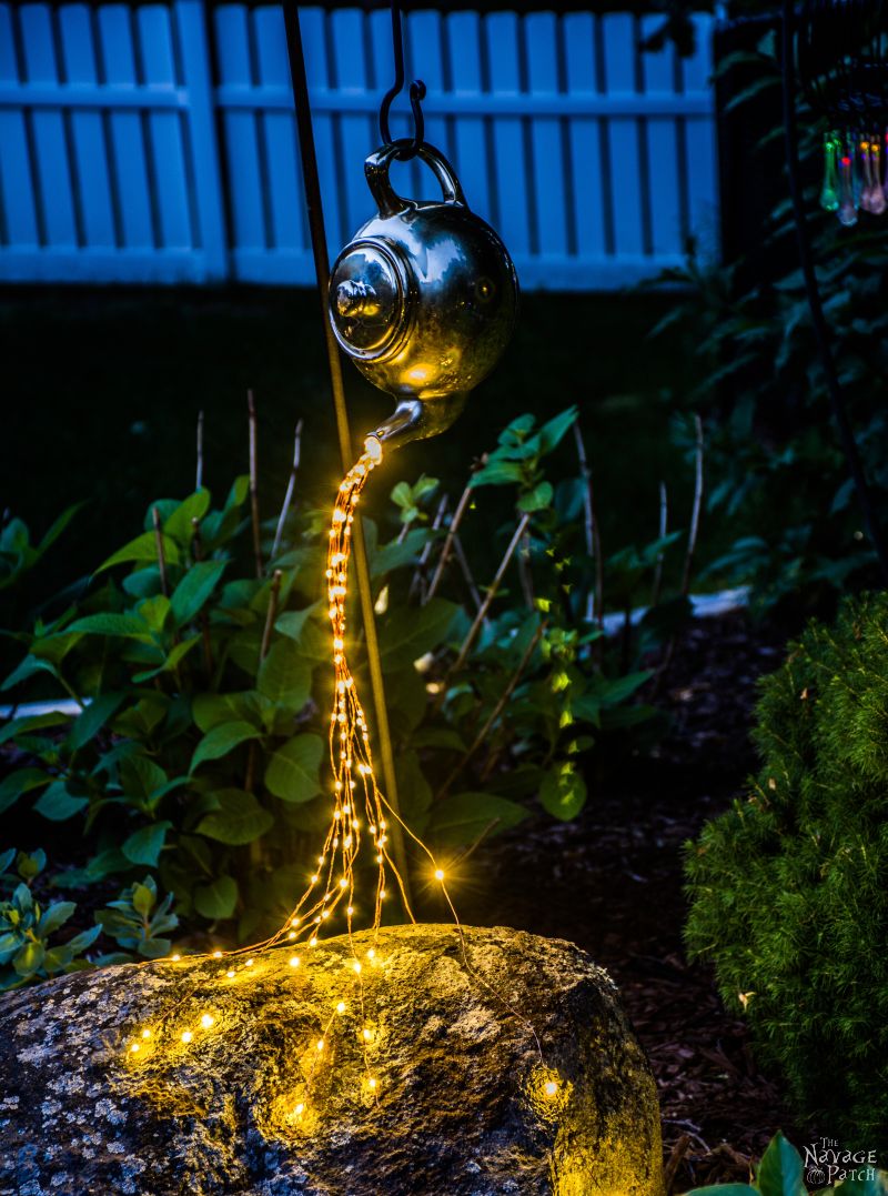 Teapot with spilling solar fairy lights in a garden at night