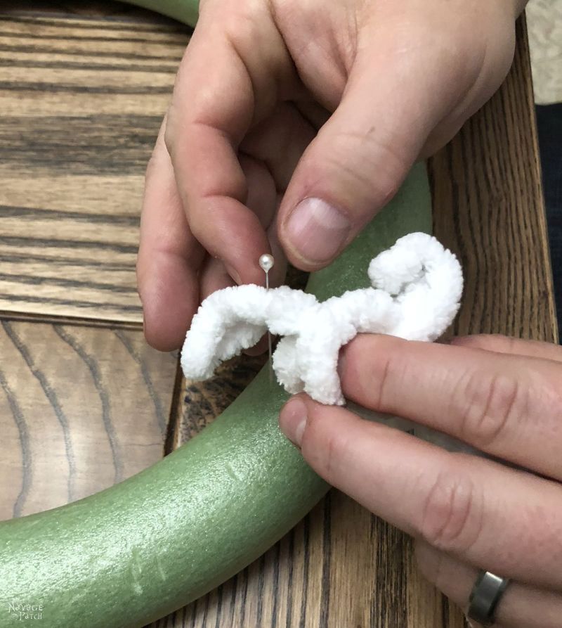 man's fingers inserting pin through yarn into wreath form