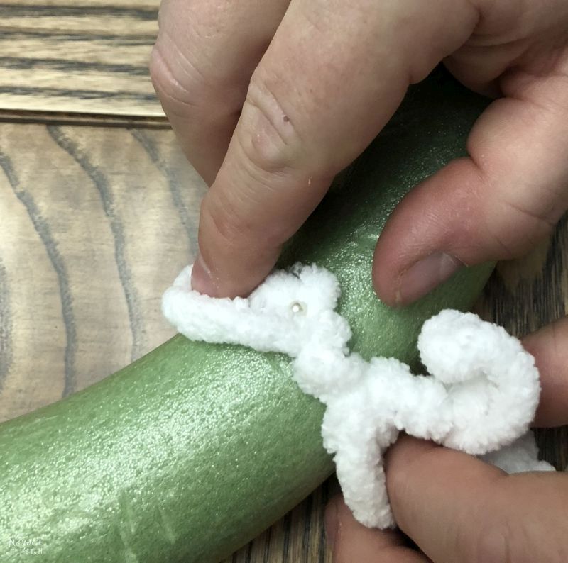 man's fingers holding loop yard against wreath form