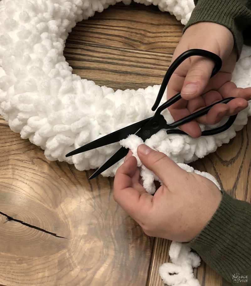 man trimming excess loop yarn from winter wreath