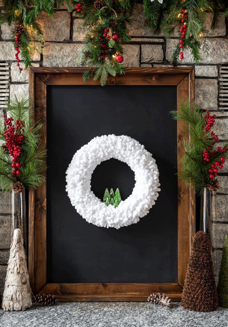DIY winter loop yarn wreath displayed in a frame on a fireplace hearth