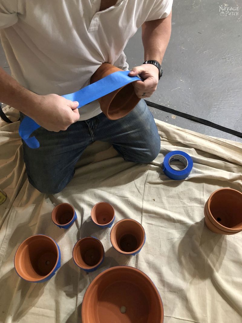 man wrapping blue tape around terra cotta pots