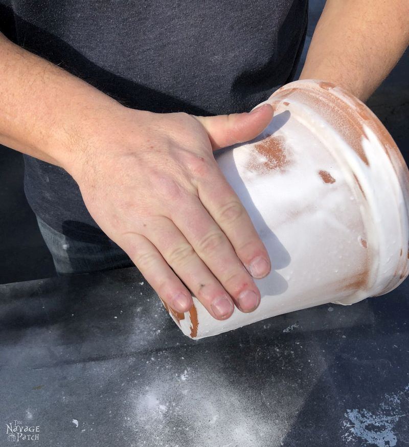 man rubbing excess baking soda from a faux aged terra cotta pot