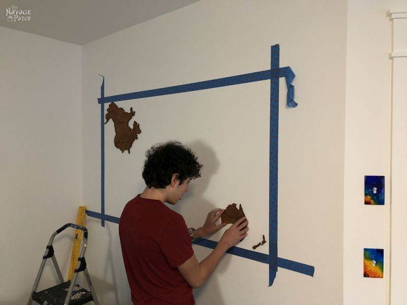 boy sticking wooden country on a wall