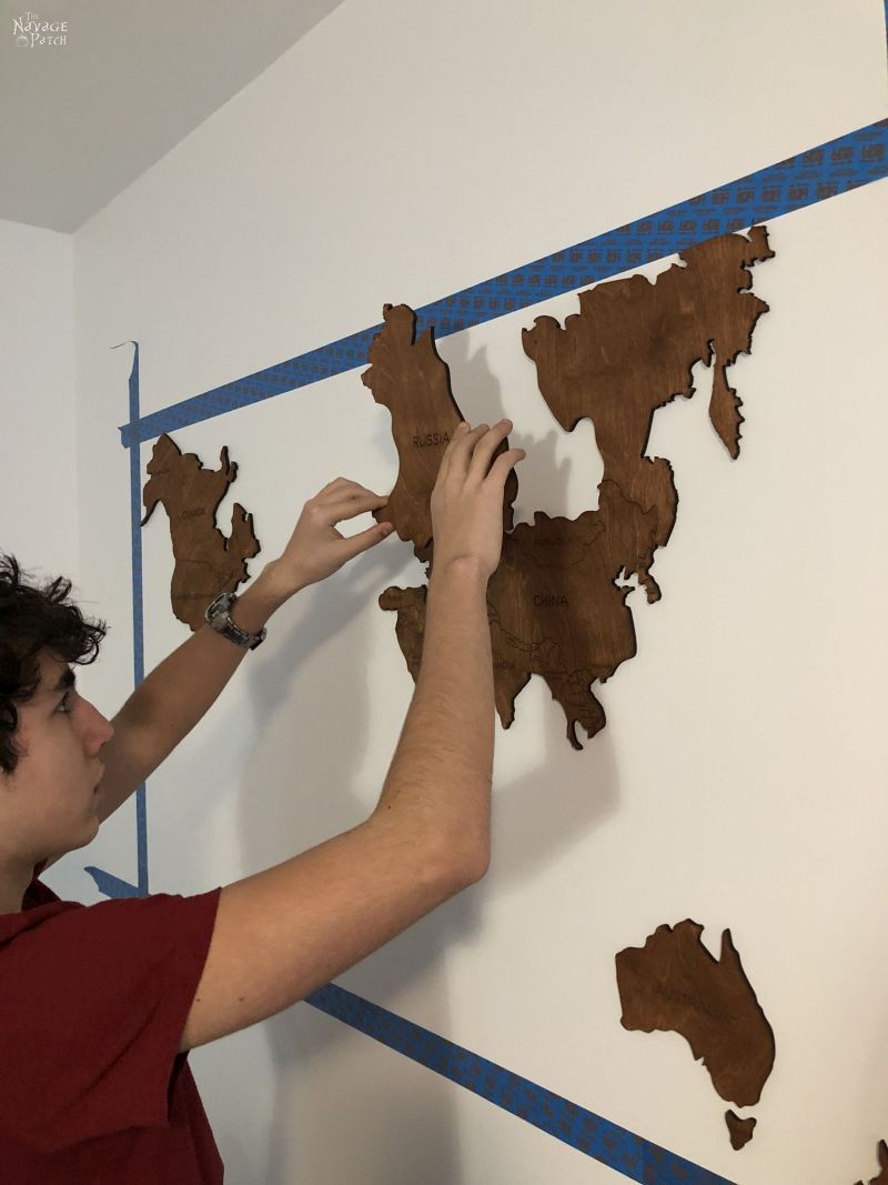 boy sticking wooden country on a wall