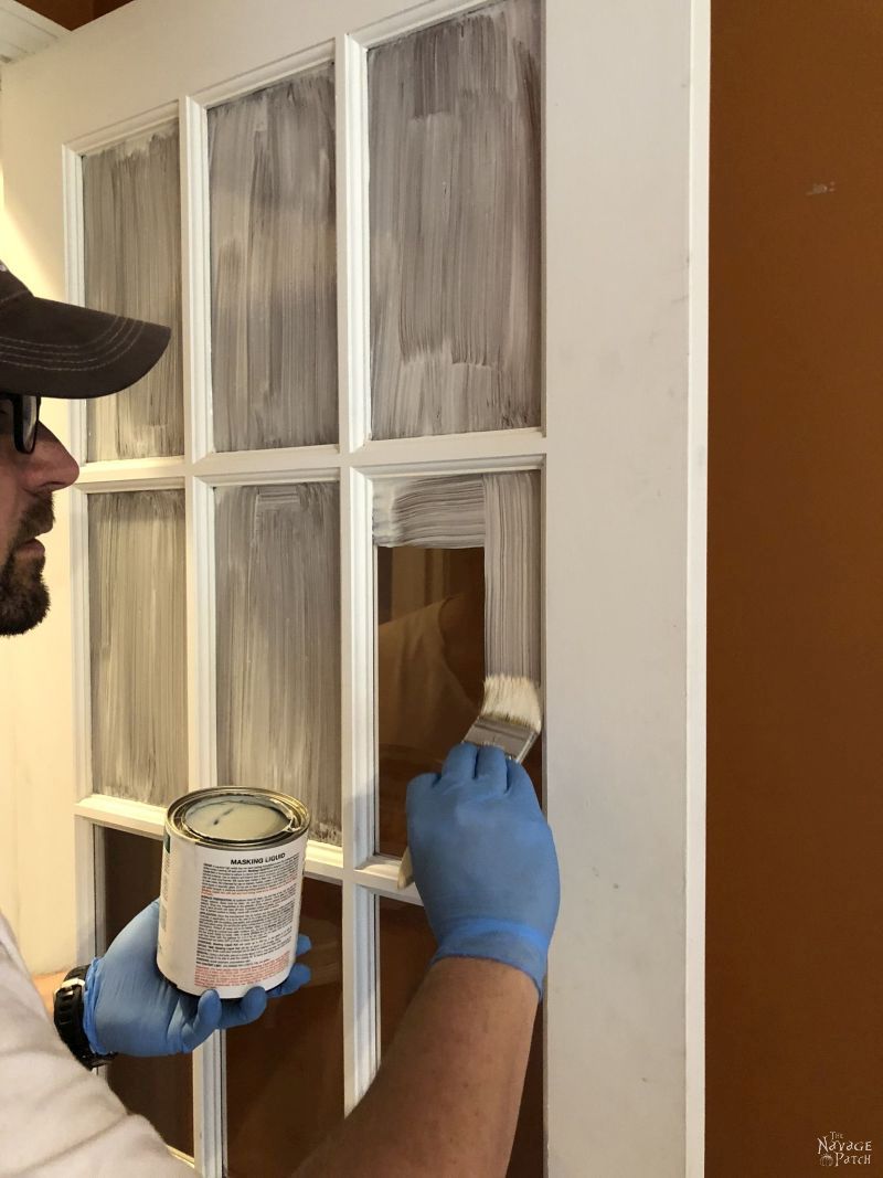 prepping to paint french doors by applying masking liquid to the panes