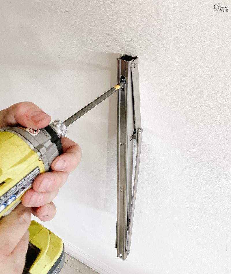 man installing a folding bracket on a garage wall