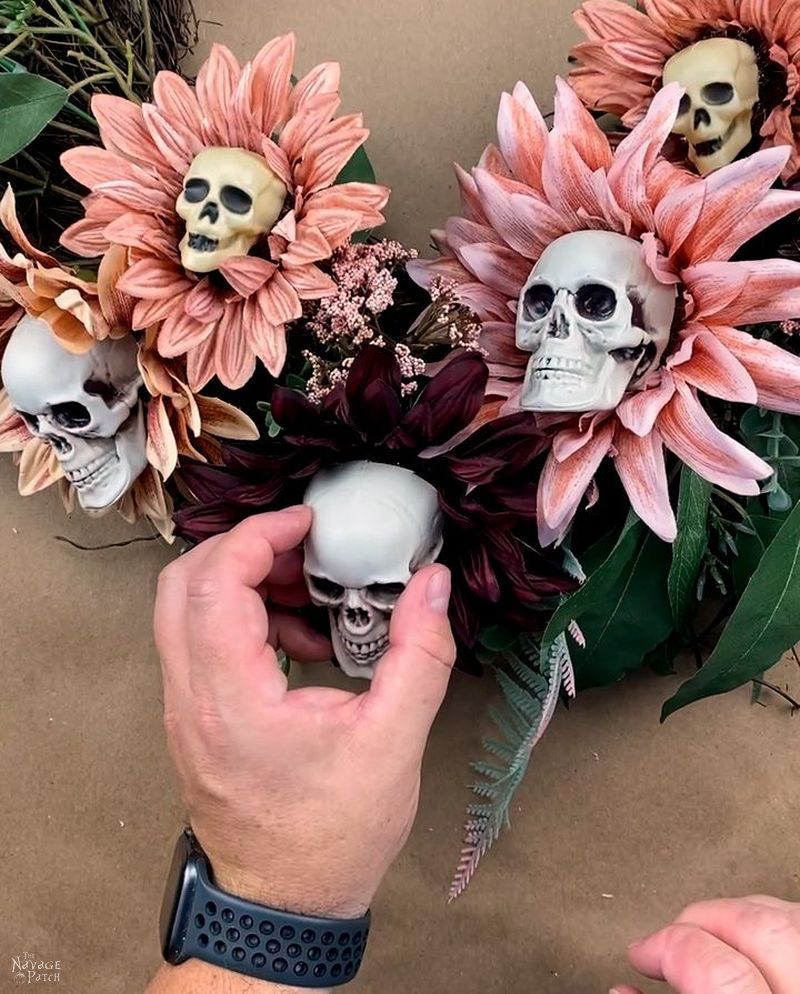 man stick a cut plastic skull with glue on it onto a sunflower on a wreath