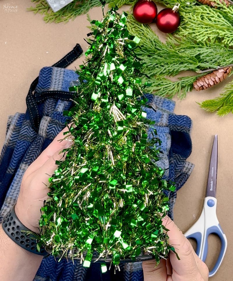 man holding cone-shaped tinsel tree