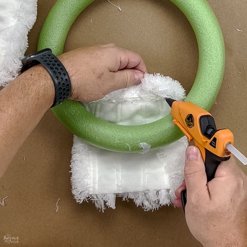 man putting hot glue on a mop head before wrapping it around a wreath form