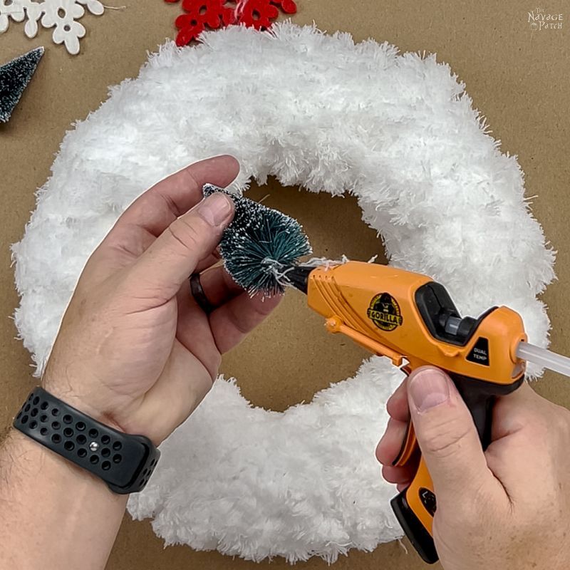 man putting hot glue on the base of a bottle brush tree