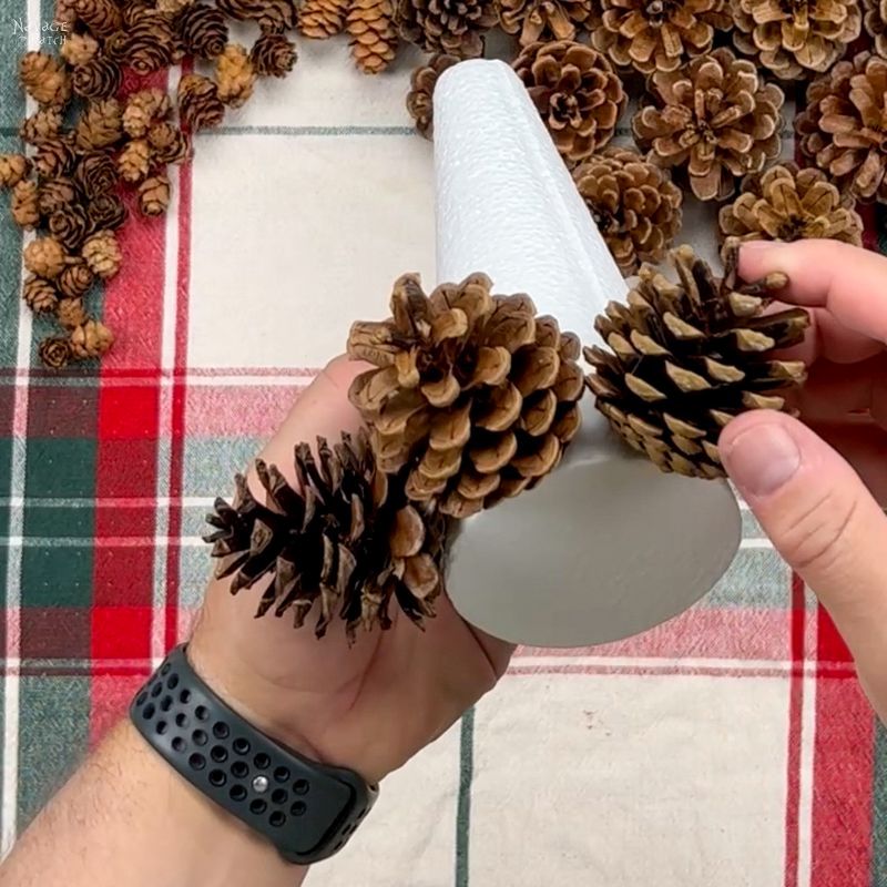 man gluing pine cones to a foam cone