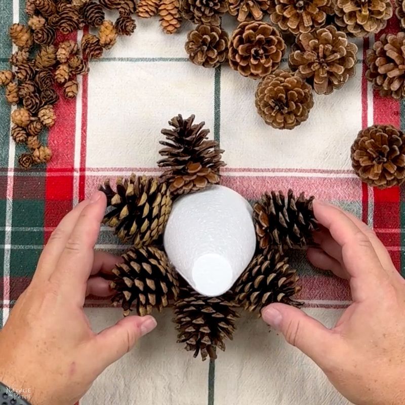 man gluing pine cones to a foam cone