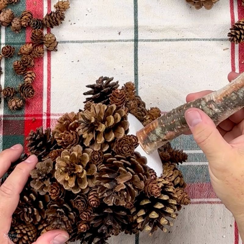 man gluing a stick to a pine cone tree