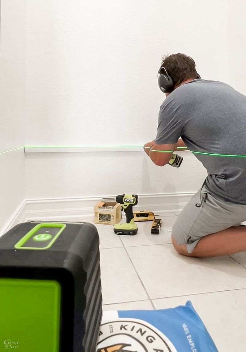man using a laser level to mount a board on a wall