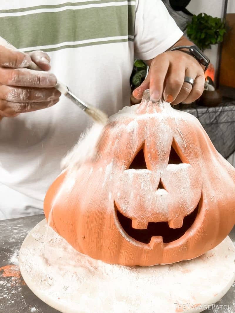 man brushing flour onto a painted pumpkin