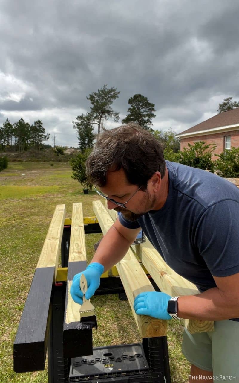 man brushing asphalt emulsion on fence posts