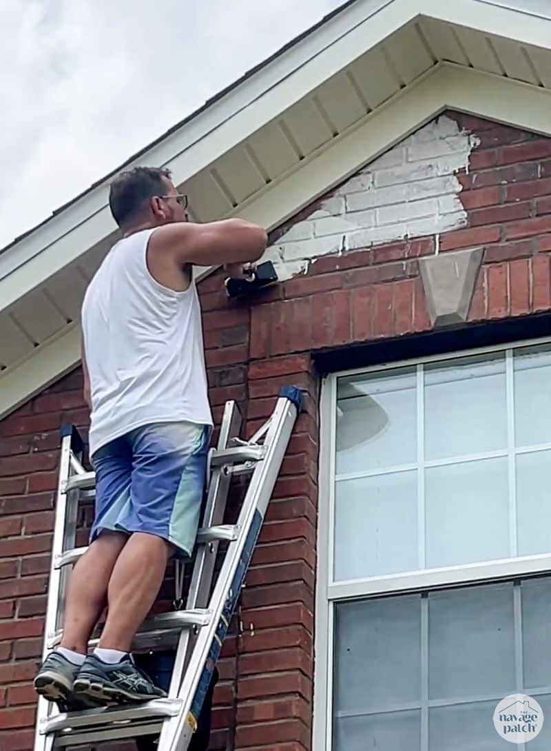 man limewashing a brick house