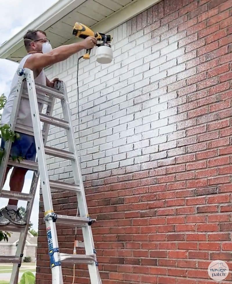 man spraying limewash paint on a brick house