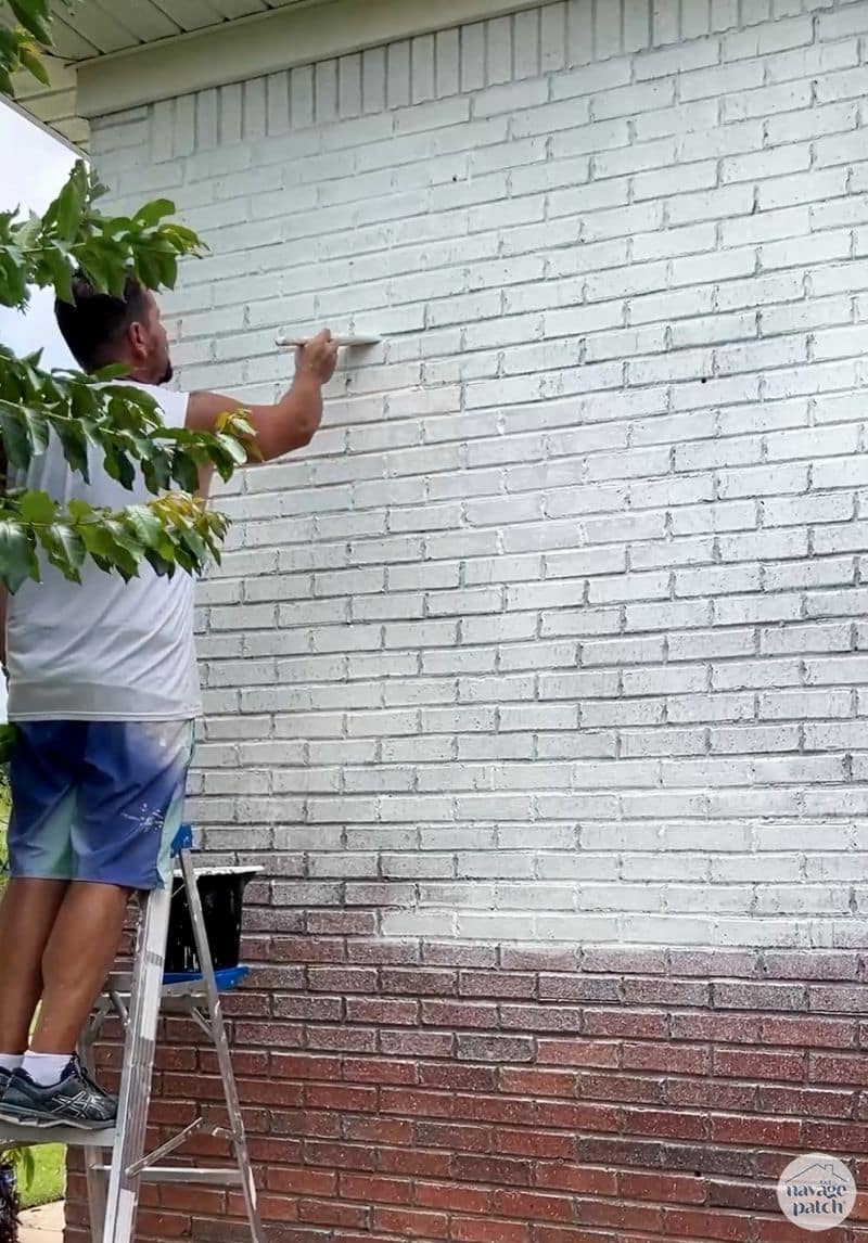 man painting limewash onto a brick house