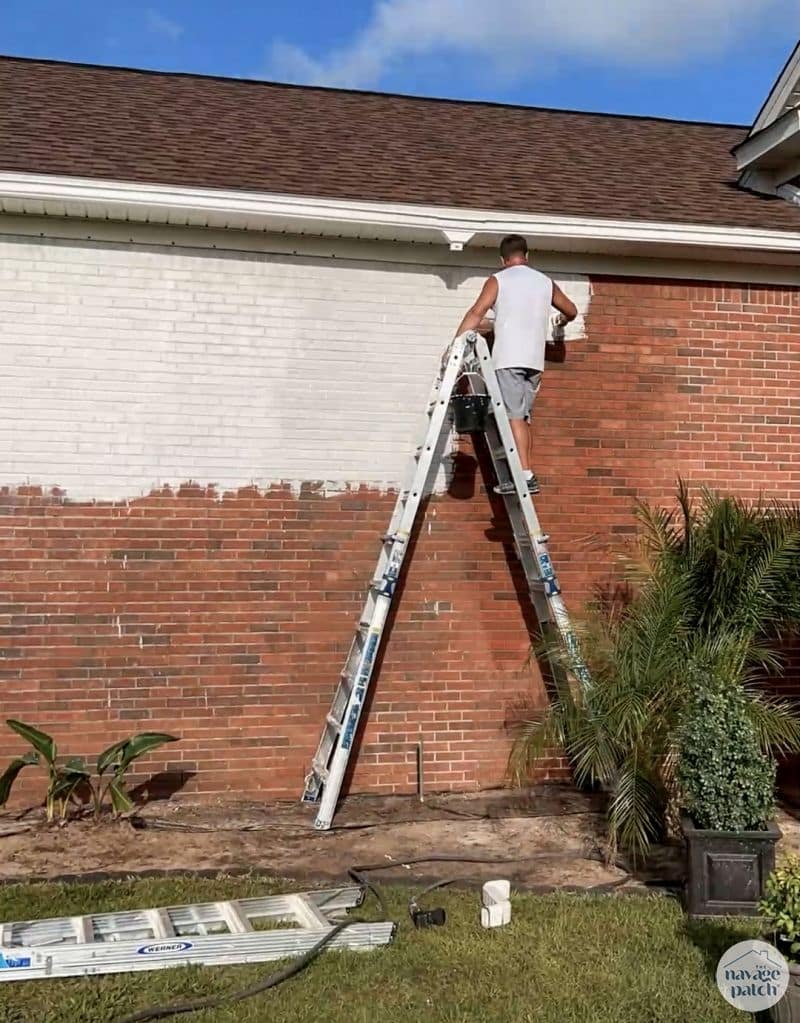 man putting limewash paint on a brick house