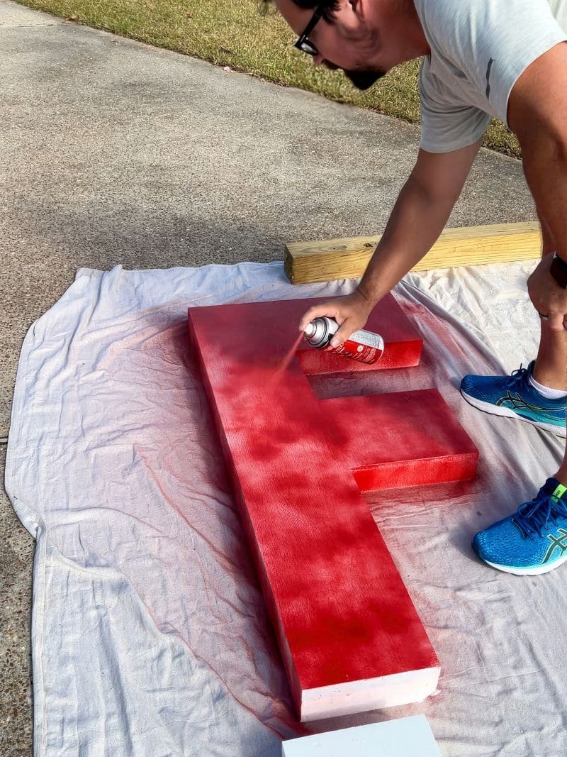 man spray painting big foam letters