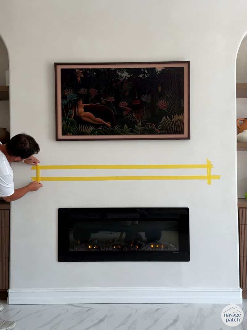 man marking a mantel placement with tape on the wall