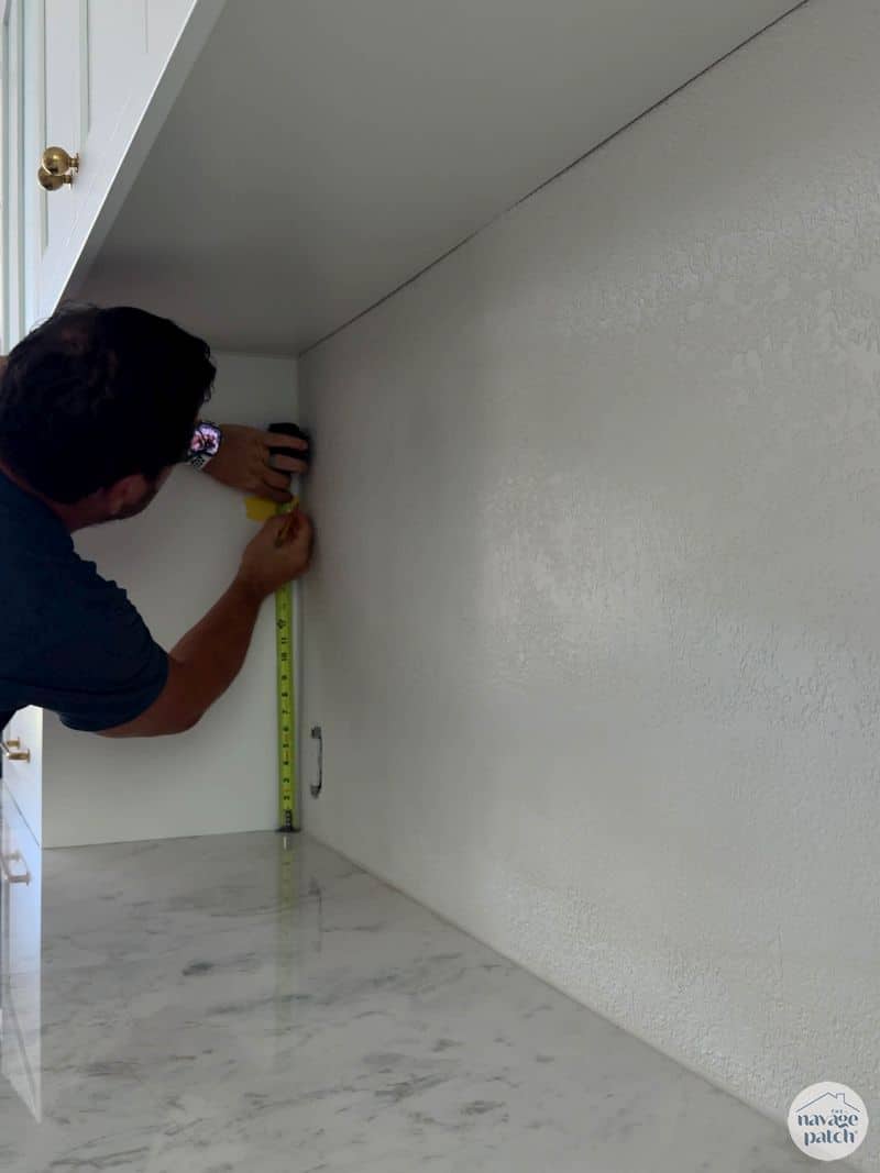 man marking shelf location on wall